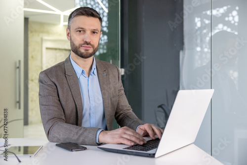 A focused professional man in a suit working intently on a laptop in a modern office setting, exuding a serious demeanor.