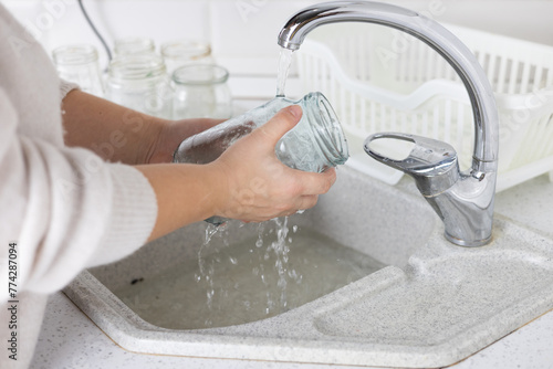 Well in the kitchen, a woman washes glass jars in the sink to sort them for recycling. The woman is responsible for saving the planet from garbage and sorts the glass and sends it for recycling.