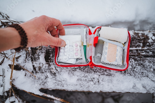 Take pills out of the first aid kit with your hand, a small compact first aid kit lying in the snow, medicines for first aid in the forest.