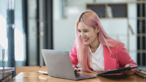 Asian business woman with pink hair is sitting at a desk with a laptop in front of her