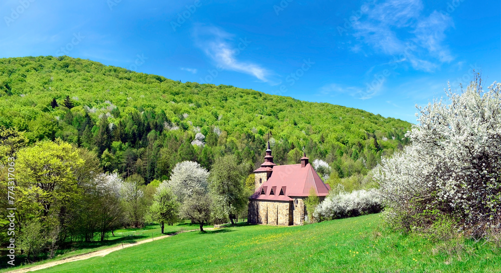 A  stone church in the picturesque landscape in Huta Polanska of the Low Beskids (Beskid Niski) in spring sunny day, Poland - obrazy, fototapety, plakaty 
