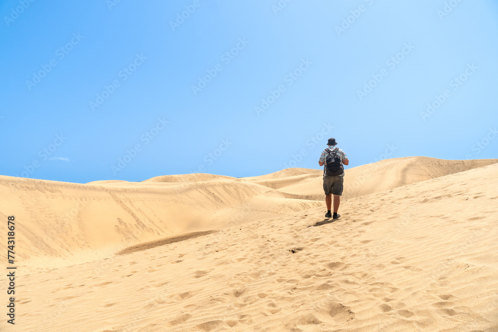 A tourist walking through the dunes of Maspalomas, Gran Canaria, Canary Islands A tourist walking through the dunes of Maspalomas, Gran Canaria, Canary Islands