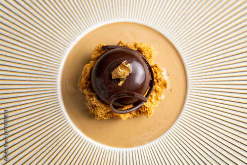 Fototapeta Naklejka Na Ścianę i Meble -  Zenithal photograph of a cherry-shaped chocolate dessert. Minimalist meals from high-quality restaurants. Gastronomic photography of frozen desserts. Brown colors predominate in the photo.