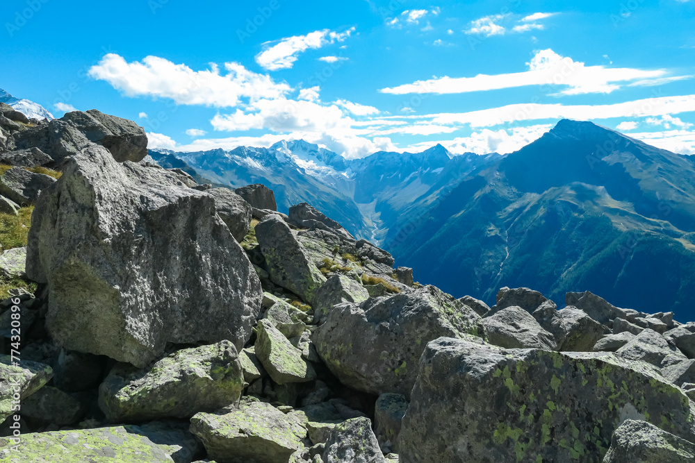 Rock formation with panoramic view of majestic snow covered mountain peaks of High Tauern National Park, Carinthia, Austria. Idyllic hiking trail over rocky scree field in summer. Remote Austrian Alps
