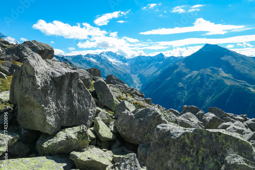Fototapeta Naklejka Na Ścianę i Meble -  Rock formation with panoramic view of majestic snow covered mountain peaks of High Tauern National Park, Carinthia, Austria. Idyllic hiking trail over rocky scree field in summer. Remote Austrian Alps