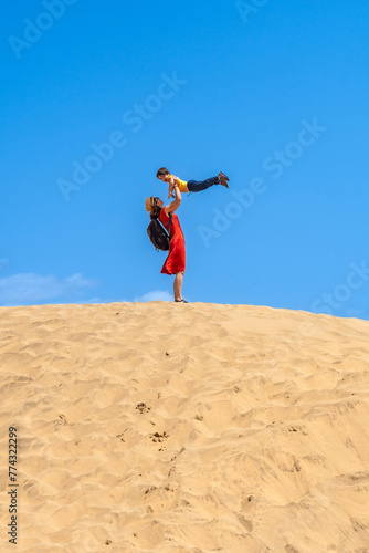 Mother lifting child smiling in the dunes of Maspalomas in summer, Gran Canaria, Canary Islands