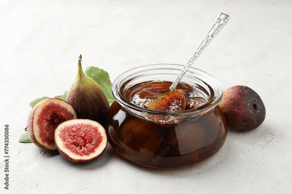 Jar of tasty sweet jam and fresh figs on white table Jar of tasty sweet jam and fresh figs on white table