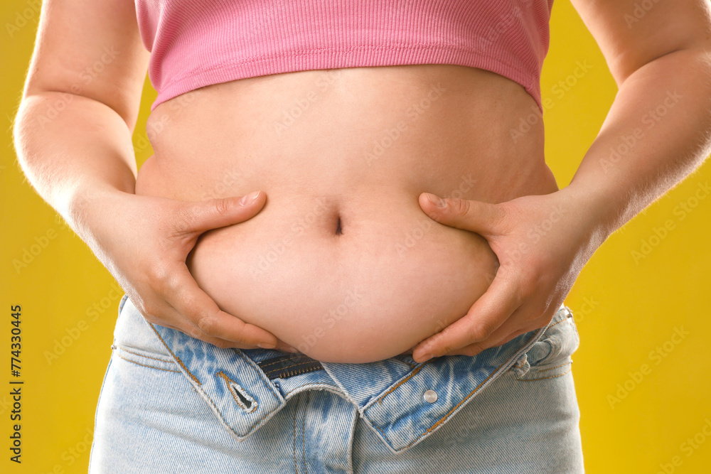 Woman touching belly fat on goldenrod background, closeup. Overweight problem - obrazy, fototapety, plakaty 