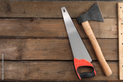 Saw with colorful handle and axe on wooden background, flat lay. Space for text photo