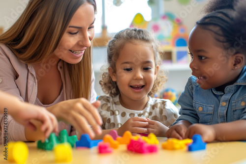 children and teacher in nursery school play with colored cubes