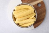 Tasty fresh yellow baby corns in bowl on white table, top view