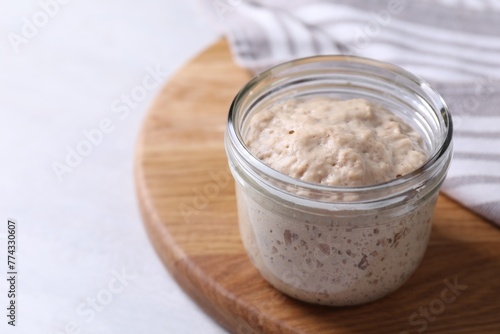 Sourdough starter in glass jar on light table  closeup. Space for text
