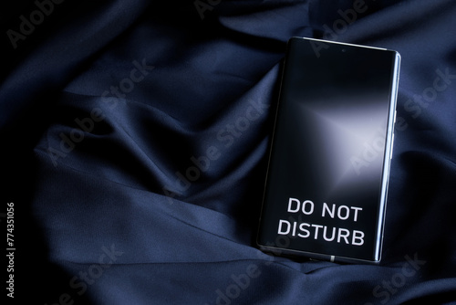 Modern smartphone with do not disturb inscription on the screen on a dark background of cosy fabric. The concept of rest and solitude of an introvert. Weekends and holidays. Photo