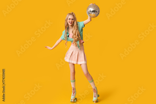 Beautiful young happy woman in vintage roller skates with disco ball on yellow background © Pixel-Shot