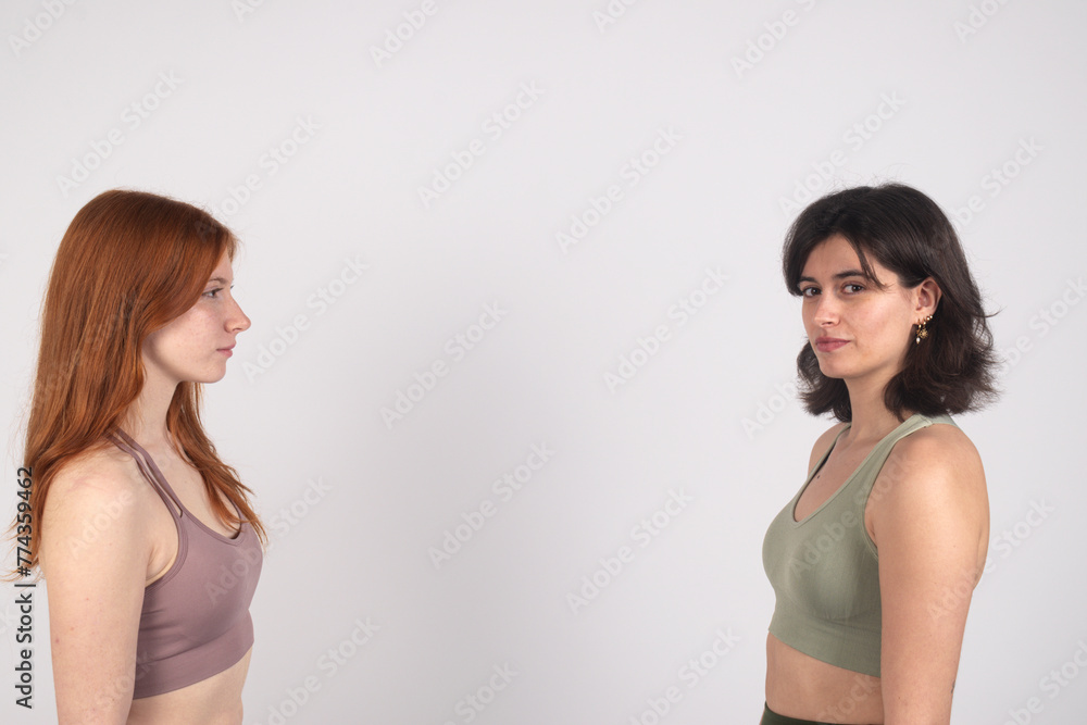 Two women facing each other against a white background, displaying neutral expressions. Two women facing each other against a white background, displaying neutral expressions.