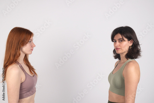 Two women facing each other against a white background, displaying neutral expressions.