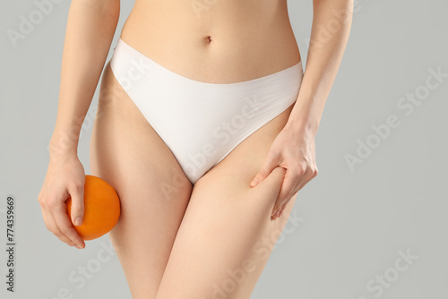 Beautiful young woman in underwear with orange on grey background. Concept of cellulite