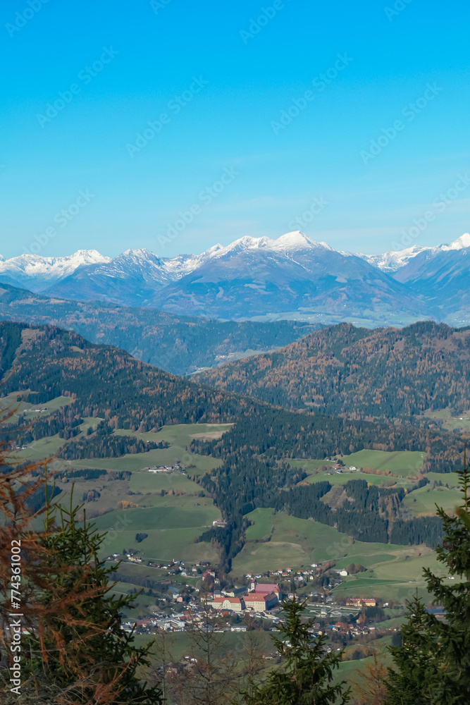 Panoramic view of alpine village St Lambrecht and snow capped mountain ridges Woelzer Tauern seen from mountain peek Grebenzen, Gurktal Alps, Styria, Austria. Calm serene atmosphere in Austrian Alps