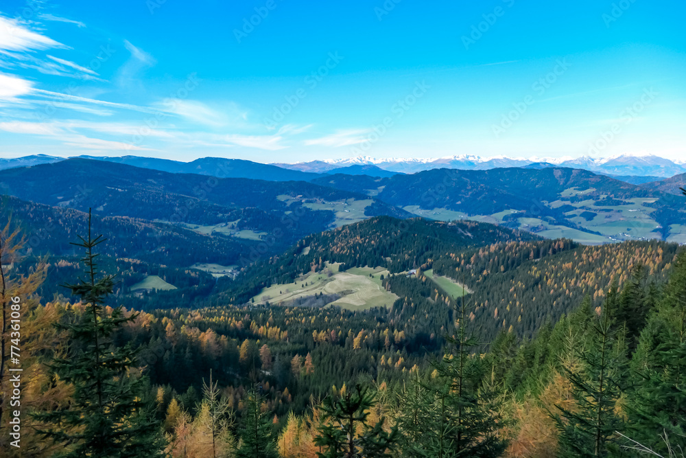 Fototapeta premium Panoramic view of snow capped mountain ridges of Woelzer Tauern seen from Grebenzen, Gurktal Alps, Styria, Austria. Calm serene atmosphere in Austrian Alps. Idyllic forest in foreground. Wanderlust