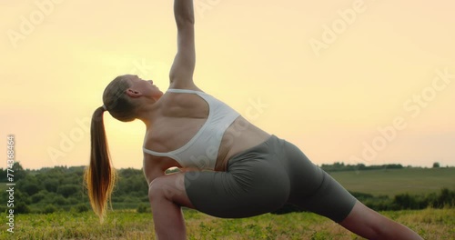 Young woman doing yoga in nature, wearing a white top and olive-colored shorts.