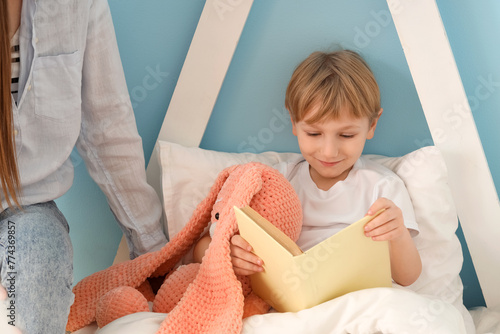 Cute little boy with his mother reading book in bed
