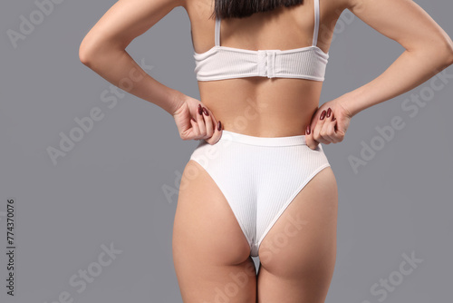 Young woman in white underwear on grey background, back view
