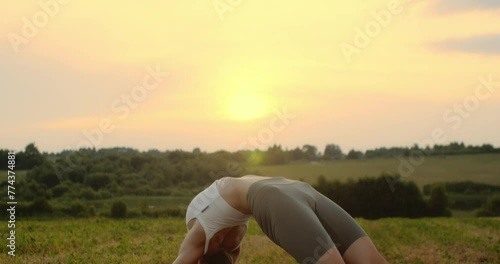 Young woman doing yoga in nature, wearing a white top and olive-colored shorts.