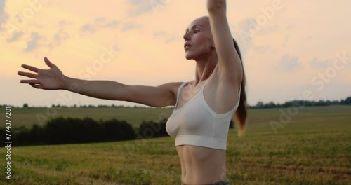 Young woman doing yoga in nature, wearing a white top and olive-colored shorts.