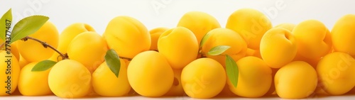 Large group of yellow plums with leaves on a white background.