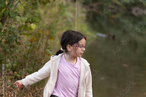 Little girl in glasses and a white coat walks in the park.