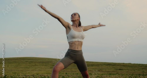 Young woman doing yoga in nature, wearing a white top and olive-colored shorts.