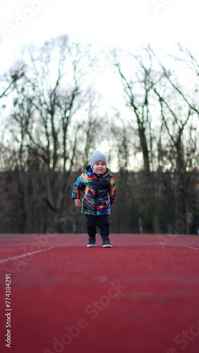 Wallpaper Mural Funny Caucasian toddler kicking the ball by the stadium track. Happy child playing outdoors in autumn. Vertical video. Torontodigital.ca