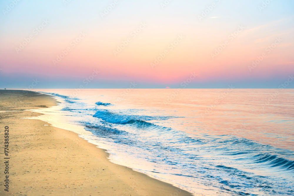 Sunset on beach with sea waves, coastline, sun and dramatic sky