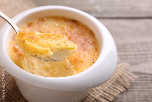 Taking delicious creme brulee with spoon from bowl at table, closeup