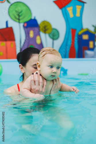 A 6-month-old boy swims in the pool. Trainer teaches baby to swim, swimming pool for children. Child development.