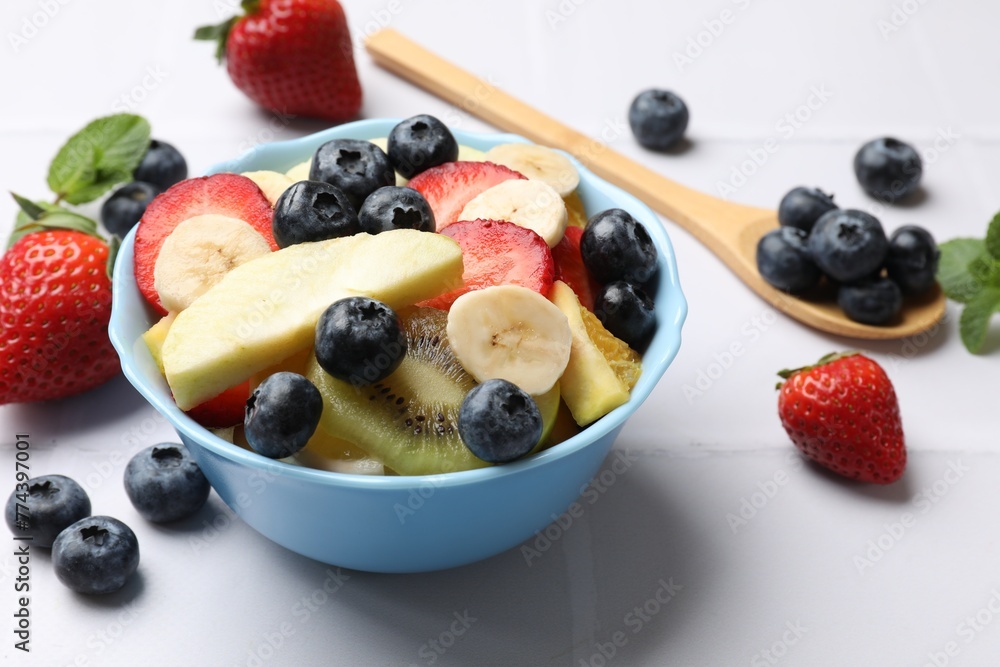 Tasty fruit salad in bowl and ingredients on white tiled table, closeup Tasty fruit salad in bowl and ingredients on white tiled table, closeup