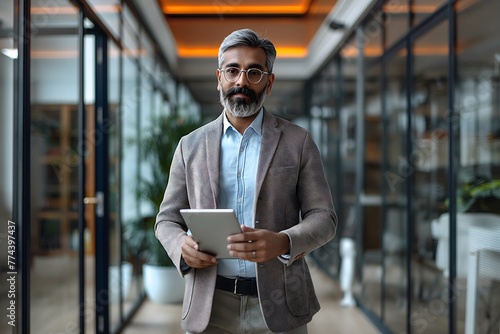 Selbstbewusster indischer Geschäftsmann, Vielbeschäftigter Geschäftsmann steht mit digitalem Tablet in den Flur, modernes Büro photo
