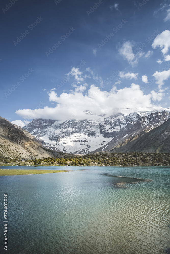 Blue mountain lake in a mountain valley among vegetation against the backdrop of rocky peaks with snow in the Fan Mountains in Tajikistan, Tien Shan highlands in the evening