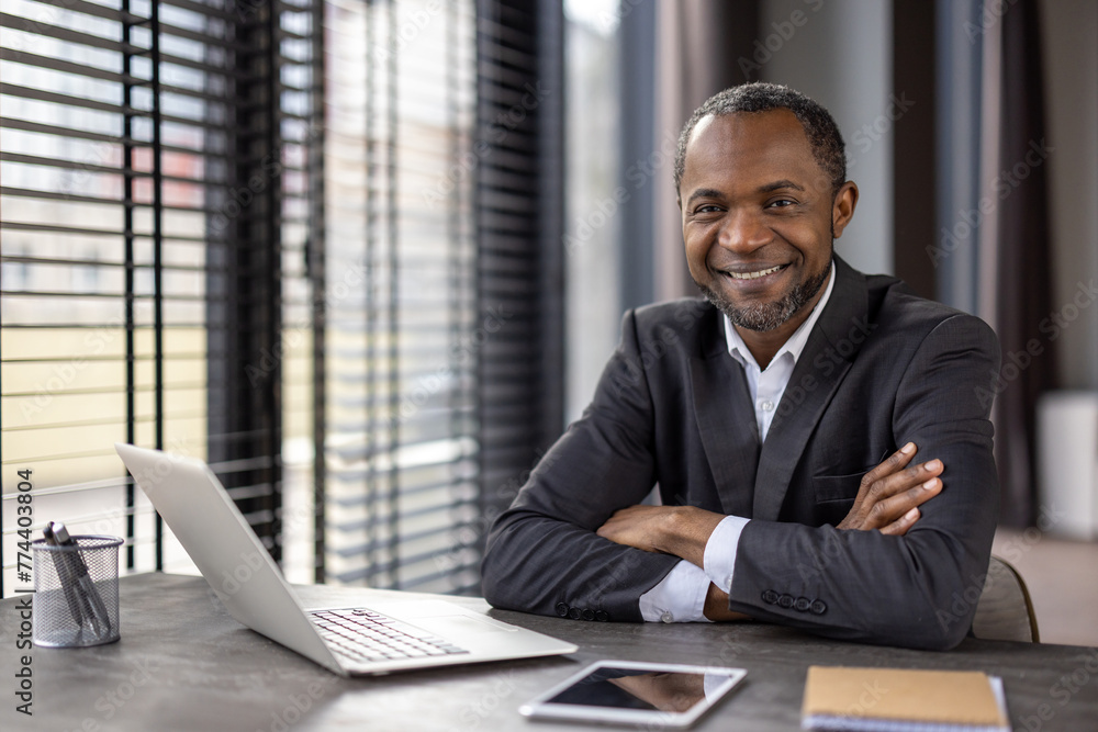 Portrait of a confident African American businessman with a warm smile sitting at his desk in a well-lit modern office setting. Portrait of a confident African American businessman with a warm smile sitting at his desk in a well-lit modern office setting.