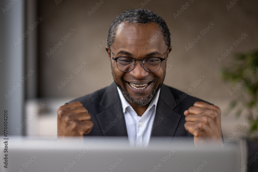 An overjoyed African American businessman celebrates a successful deal or achievement while working on his laptop. An overjoyed African American businessman celebrates a successful deal or achievement while working on his laptop.