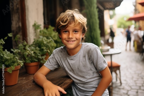 Portrait of a cute little boy with blond hair in a gray T-shirt sitting in a cafe and smiling