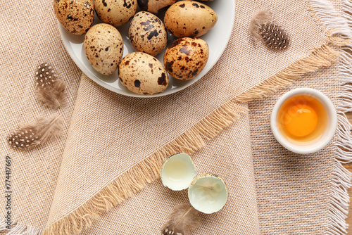 Plate with fresh quail eggs and feathers on napkin