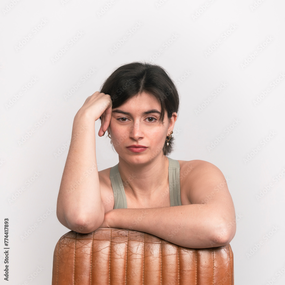 A woman leans on a brown leather chair, looking directly at the camera, against a white background. A woman leans on a brown leather chair, looking directly at the camera, against a white background.