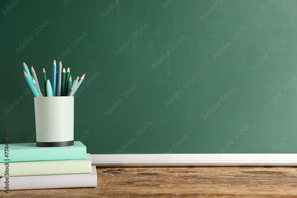 Pencil holder full of pencils and books on table against green background. End of school Pencil holder full of pencils and books on table against green background. End of school