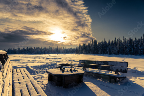 Une table brasero et deux bancs devant une forêt et une étendue de neige au lever du soleil en Laponie en Suède