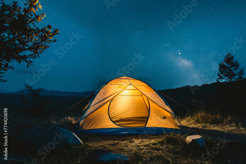 A small tent lit from within during the nighttime at a campsite