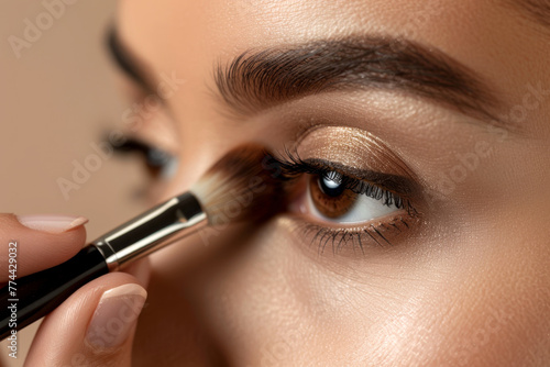 Woman's eye as she applies shimmering eyeshadow with a brush.