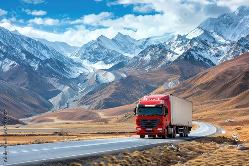 Red semi truck driving on scenic asphalt road through breathtaking snow-capped mountain landscape photo