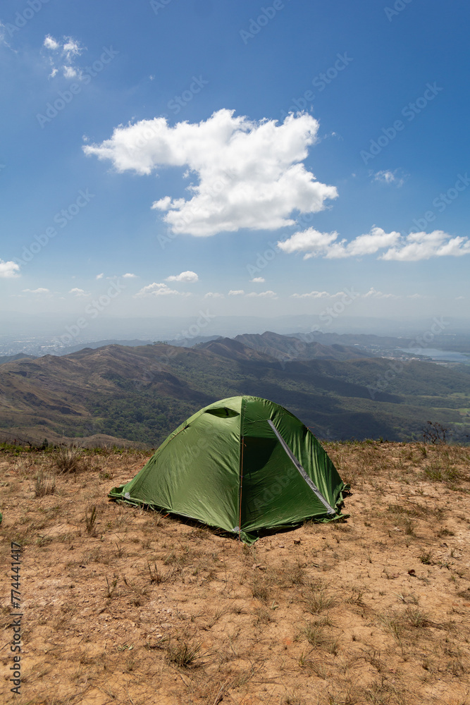 Green camping tent on top of mountain with amazing view of mountain range on background. Time spending on fresh air. Traveling concept.