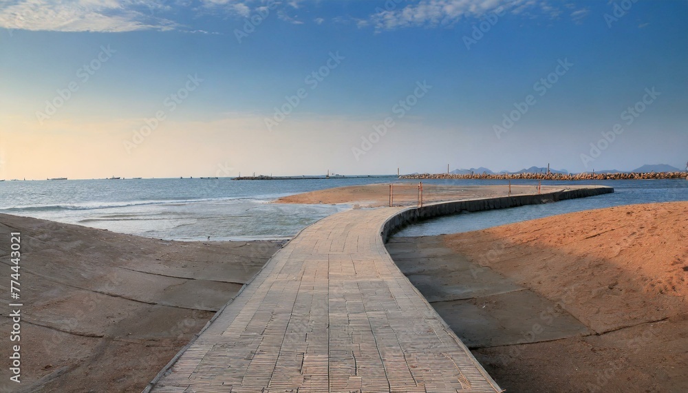 Textured stone barriers line the tranquil path that offers an expansive view of the sea and distant city under a soft evening light